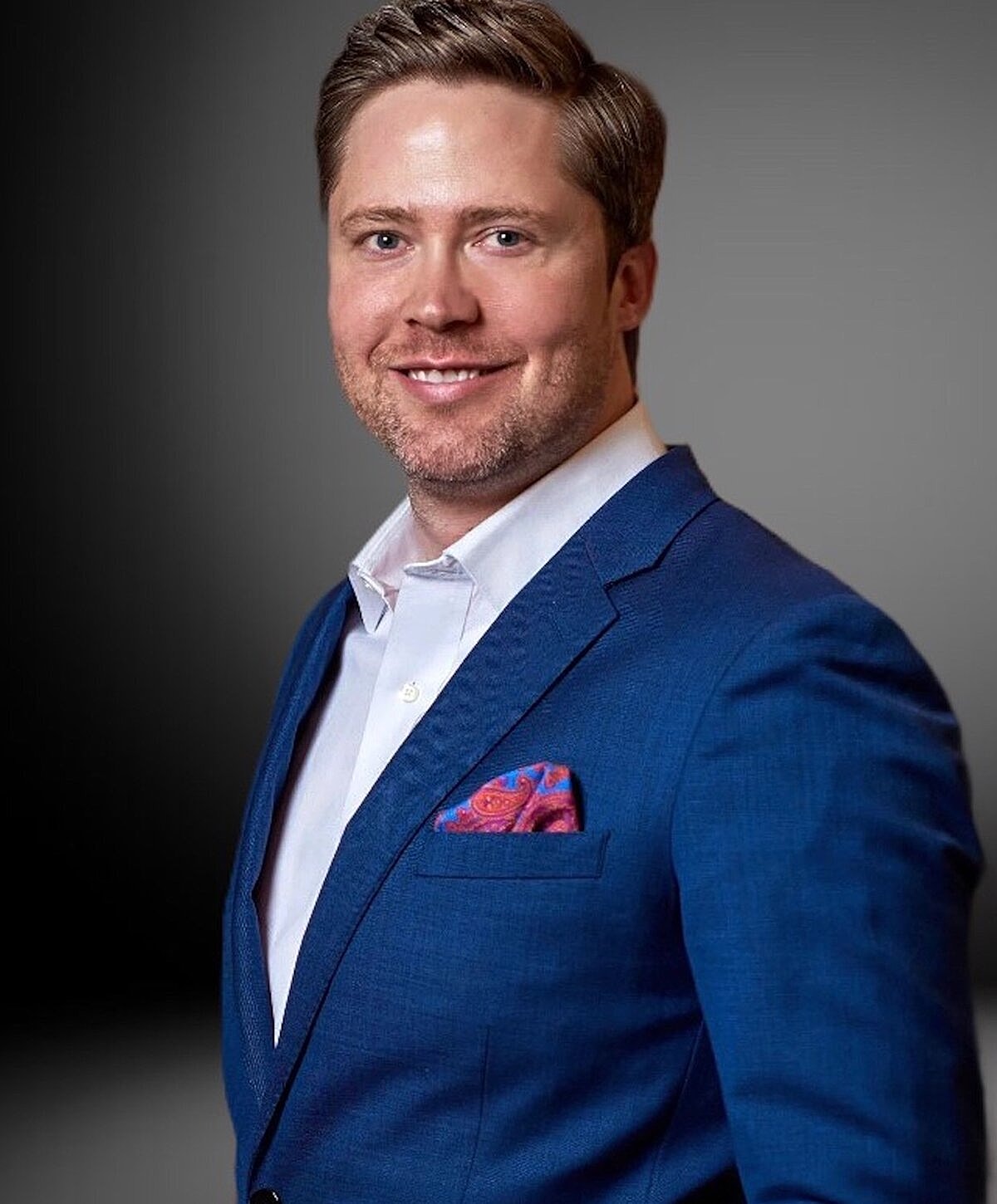 Man in blue suit smiling confidently.