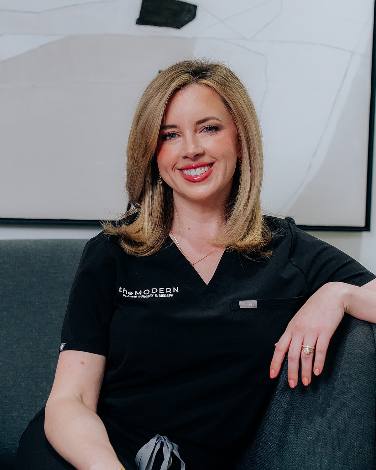 Smiling woman in medical attire sitting comfortably.