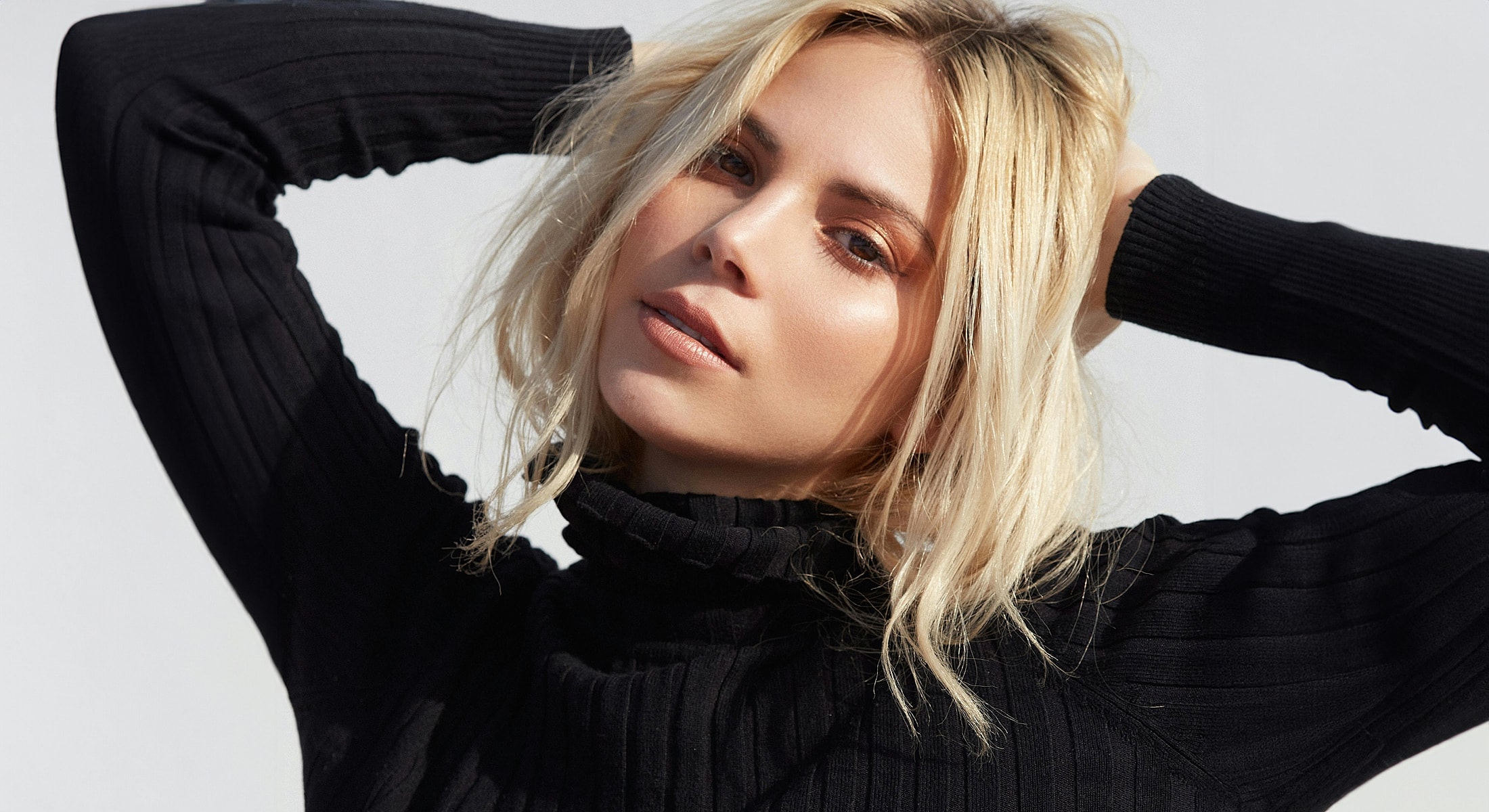 Woman with blonde hair posing in black sweater.