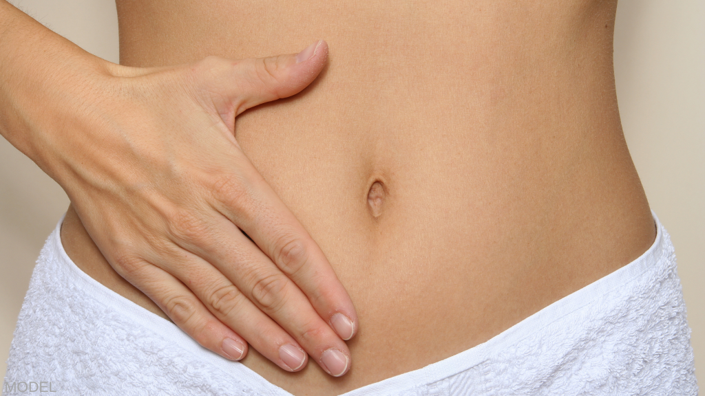 Woman with towel around her waist and hand on stomach. (MODEL)