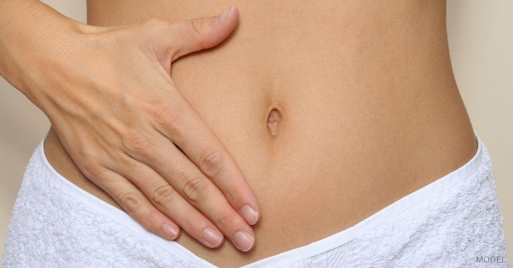 Woman with a hand on her stomach and a towel around her waist. (MODEL)